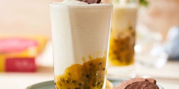 En krämig dessert i ett glas med ett lager passionsfruktskött, toppad med ett chokladkex, serverad på en tallrik med extra kex.