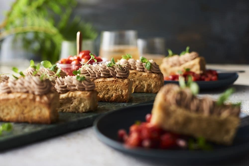 Kakskivor toppade med chokladglasyr och garnerade med microgrönt, serverade på mörka tallrikar med suddig bakgrund.
