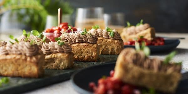 Kakskivor toppade med chokladglasyr och garnerade med microgrönt, serverade på mörka tallrikar med suddig bakgrund.